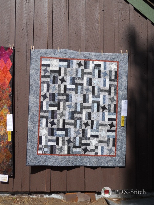 photograph showing a grey, black, and white striped quilt with black and grey star appliques at the Sisters Quilt Show
