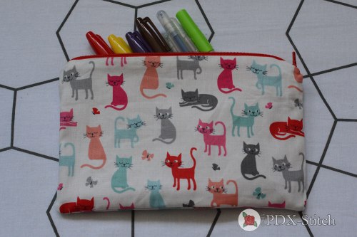 picture of zippered pouch made from colorful cat-printed fabric with red zipper, with markers and pens spilling out