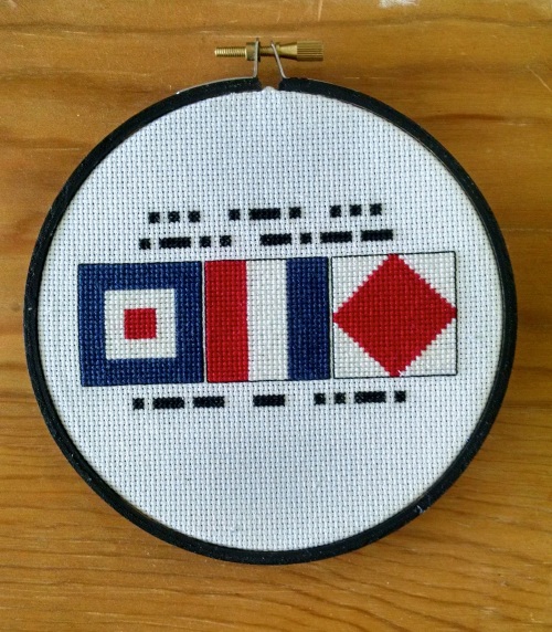 picture of cross stitched embroidery hoop with the nautical signal flags for whiskey (W), tango (T), and foxtrot (F), spelling "WTF"