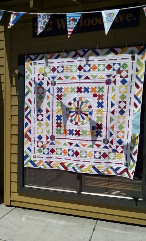 Quilt with white background and simple geometric shapes in many bright colors.
