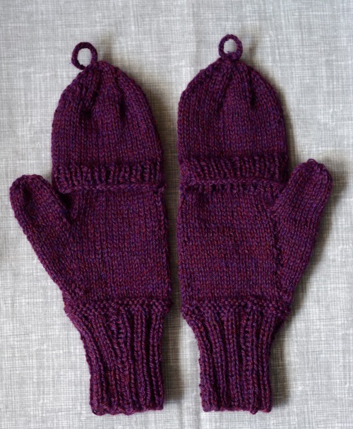 A pair of purple knitted mittens side by side on a gray checkered background, palm side up.