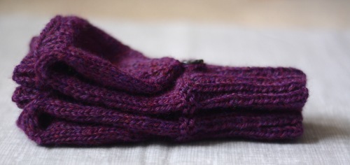 A pair of purple knitted mittens stacked on top of each other, shown from the side